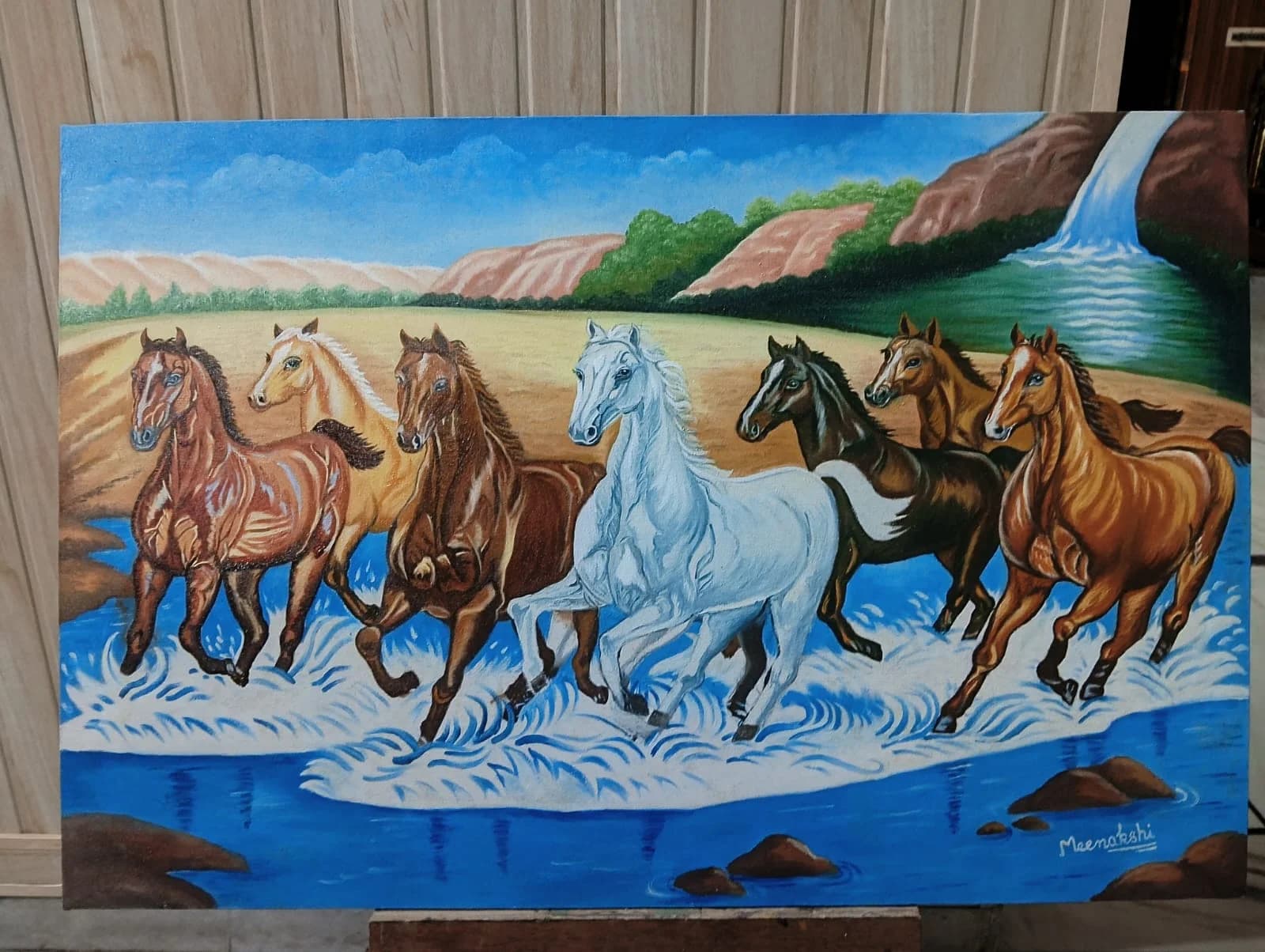 Seven horses crossing a river beneath a waterfall and canyon cliffs